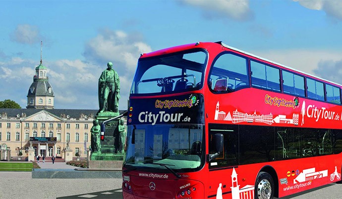 Ein roter Doppeldeckerbus fährt vor dem Schloss entlang 